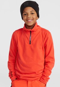 Fleece-pullov i stark orange med hög krage och dragkedja i halsen. Har svart logotyp på placket och ärmarna.