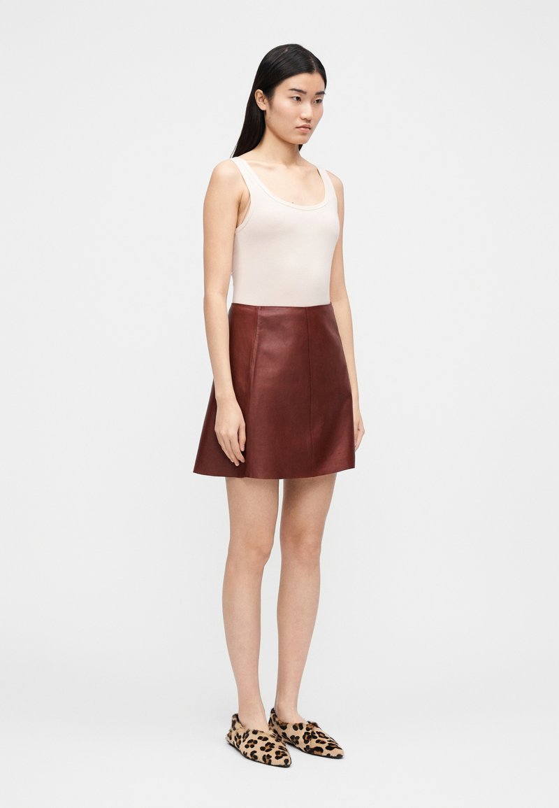 Lædernederdel i bordeaux, figursyet talje, skørt med vidde. Kombineret med en beige tanktop og slip-on sko med leopardmønster.