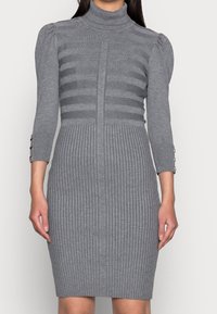 Robe gris tricotée avec col roulé, présentant une texture à rayures horizontales sur le buste et un côtelé vertical sur la jupe, manches trois-quarts.