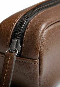 Rjava usnjena torba z teksturirano površino, ki ima črn zadrgo in kovinski poteg, ter natančno šivanje ob robovih.