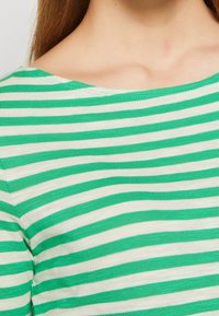 Lähiotoksia ylävartalosta, jossa on vihreä ja valkoinen vaakaraidallinen paita, näyttää kaula-aukon ja solisluun alueen.