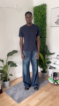 Navy cotton t-shirt with pocket, paired with light blue wide-leg jeans. Black shoes, indoor setting with greenery and soft gray rug.