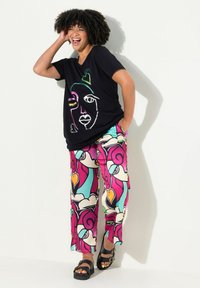 Zwarte t-shirt met een kleurrijk abstract gezichtsontwerp, gecombineerd met levendige, gestreepte wijde broek met roze, paarse en turquoise wervelingen en harten.