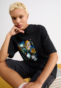 Black T-shirt featuring colorful graphic design with various motifs, including dice, a rose, and hand illustrations; soft cotton material.