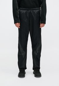 Mustad mustad spordipüksid, millel on kerge, sädelev tekstuur, diagonaalsed läikivad aktsendid külgedel ning elastne vöökoht.