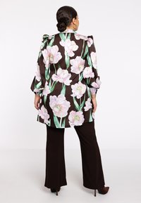 Schwarze Blazerjacke mit großen rosa Pfingstrosenmuster, leicht gepufften Ärmeln und einer Länge bis zur Mitte des Oberschenkels. Kombiniert mit dunklen Hosen und Absatzschuhen.