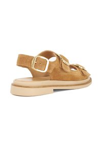 Suede sandal in tan with a raised sole, featuring a thick strap and golden buckle accents. Open back design with smooth interior.