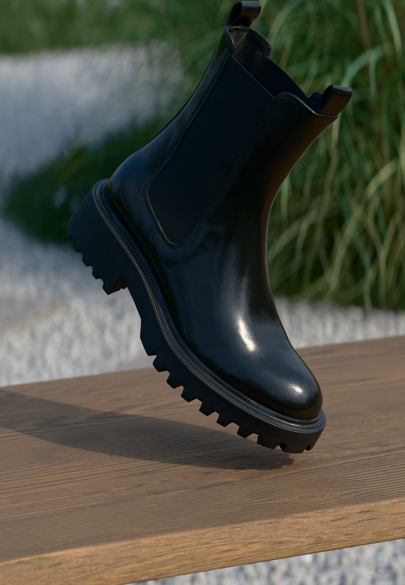 Botín Chelsea negro brillante con suela texturizada y robusta, y paneles laterales elásticos, mostrado en el aire sobre una superficie de madera.