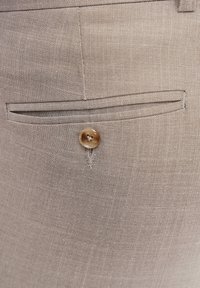 Beżowe spodnie tailored z płaską kieszenią i brązowym guzikiem, wykonane z teksturowanej tkaniny tkanej.