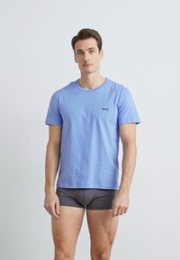 Lys blå bomull T-skjorte med rund hals og liten svart "BOSS"-logo, kombinert med grå boxershorts. Enkel design, kort erm.