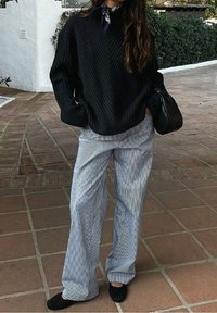 Black ribbed sweater with a high neckline, paired with light blue and white striped wide-leg pants and black flat shoes. Black handbag included.