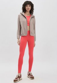 Beige fleece zip-up jack, een kort roze tanktop en nauwsluitende roze legging, gecombineerd met bruine en crèmekleurige sneakers.