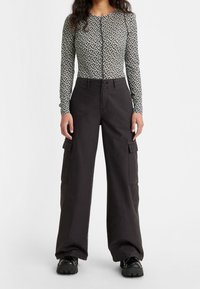 Zwarte cargobroek met zijzakken en een losse pasvorm, gecombineerd met een lange mouwen, bloempatroon, geknoopte top in zwart en wit.