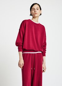 Sweat-shirt rouge à coupe décontractée, col rond et intérieur du col blanc. Associé à un pantalon rouge ample avec une taille à cordon de serrage.