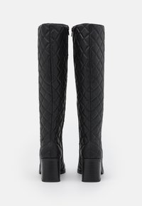 Bottes noires montantes en simili cuir matelassé, avec un talon carré et une fermeture éclair à l'arrière. Motif en losanges texturé sur toute la surface.