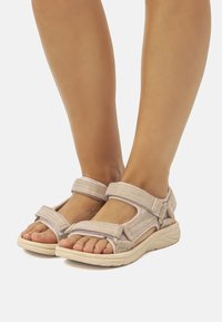 Infradito beige chiaro realizzate in tessuto testurizzato con cinturini regolabili e una suola imbottita, dotate di design aperto all'esterno e vestibilità sicura.