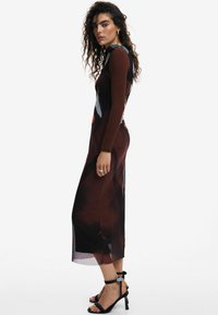 Rochie lungă, mulată, dintr-u material maro închis, cu un model abstract colorat. Secțiune de fustă transparentă, asociată cu tocuri negre cu curele.