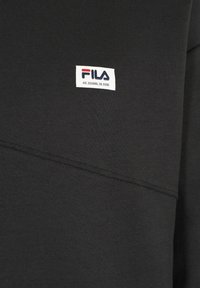 Felpa nera con cucitura diagonale, texture morbida e etichetta con logo Fila con coordinate. Design semplice e dettagli minimi.