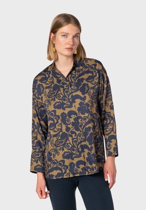 Printed shirt featuring a floral design in navy on a tan background, with a collar, buttons, and long sleeves. Smooth fabric texture.