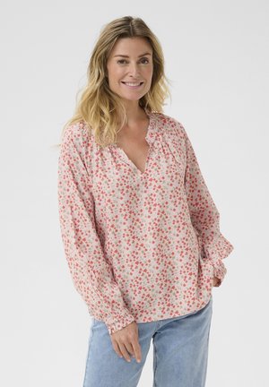 Blusa floreale in tessuto leggero, presenta un collo a V, arricciature lungo le spalle e polsini elasticizzati. I colori predominanti sono il rosa e il rosso.