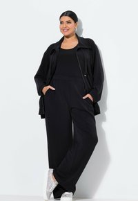 Zwart sportoutfit met een ritsjack, losse broek en slip-on schoenen met zilveren accenten. Glad materiaal en comfortabele pasvorm.
