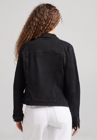 Black denim jacket with a classic cut, featuring a collar, long sleeves, and buttoned cuffs. The fabric has a smooth texture and minimal seams.