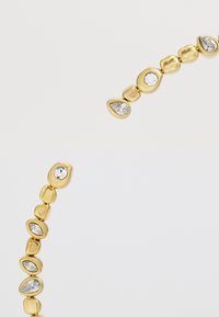Bijoux en ton doré présentant une série de formes arrondies et de pierres claires et étincelantes, alternant dans un design fluide. Texture lisse avec des surfaces réfléchissantes.