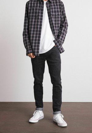 Koszula w czarno-szary bez wzoru w kratę, biała koszulka typu crew neck, ciemne dżinsy, białe trampki z czerwonymi akcentami, prezentowane na neutralnym tle.