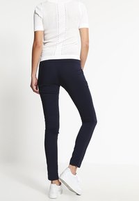 Marineblauwe slim-fit broek gemaakt van rekbaar materiaal, met een gladde textuur en een enkel-lange snit. Gecombineerd met een witte gebreide top met korte mouwen.