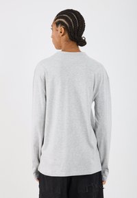 Cămașă gri cu mânecă lungă, realizată dintr-un material moale, cu guler rotund, croi lejer și un design minimalist. Vedere din spate fără logo-uri vizibile.