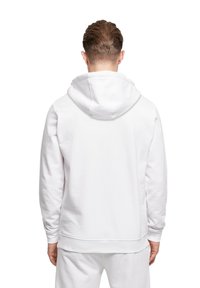 Hvid hættetrøje med lange ærmer og struktureret stof. Har en afslappet pasform og ribbede manchetter. Bagfra, ren design.