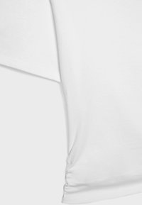 Close-up of a white short-sleeve shirt showing fabric texture and side ruching detail near the hem.