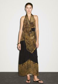 Robe longue aux tons sombres ornée d'un motif abstrait doré et brun. Le tissu tombe élégamment. Conçue avec un col halter et une silhouette longue jusqu'au sol.