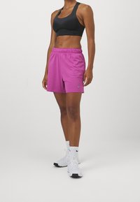 Pantaloncini sportivi viola con vita elastica, abbinati a un reggiseno sportivo nero testurizzato e scarpe da ginnastica bianche con dettagli neri e calzini bianchi.