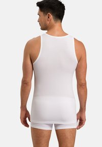 Bílý bavlněný top bez rukávů s přiléhavým střihem, featuring kulatým výstřihem a širokými ramínky, doplněný o bílé šortky.