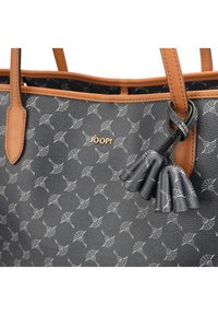 Sac en cuir gris avec un motif répétitif, des accents beige et un logo doré. Comprend un détail de frange sur le côté.
