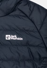 Giacca puffa blu marina con texture trapuntata e un logo bianco che presenta un'impronta di zampa sul lato sinistro. Materiale leggero, resistente all'acqua.