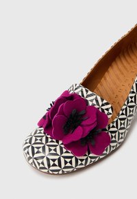 Textile loafers with a geometric black and white pattern, accented by fuchsia and black felt flowers on the upper. Brown interior lining.