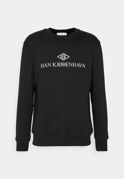 Hanorac negru din bumbac, cu guler rotund și manșete ribbate. Pe față este inscripția "HAN KJØBENHAVN" în litere albe.
