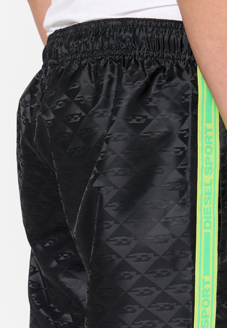 Primo piano di pantaloni sportivi neri con motivi geometrici e una striscia laterale verde neon etichettata "Diesel Sport."