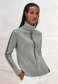 Hellgrauer Pullover mit hohem Rollkragen, schwarzen Seitenstreifen, geripptem Saum und Bündchen, ausgestattet mit einem strukturierten Strickmuster.