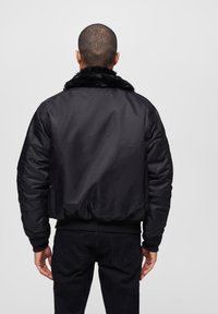 Chaqueta bomber negra con cuello de piel sintética, diseño acolchado, puños y dobladillo acanalados, y textura exterior suave. Llevada sobre jeans negros.