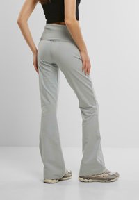 Pantaloni a zampa leggera grigi chiari con una cintura alta, realizzati in tessuto morbido, indossati con scarpe da ginnastica beige. La vista posteriore mostra una vestibilità rilassata.