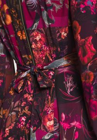 Robe fleurie en bordeaux riche avec une fermeture éclair et une ceinture en tissu. Motifs floraux vibrants dans des tons d'orange et de rose sur un tissu lisse.