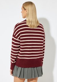 Maglione a righe bordeaux e crema con una vestibilità comoda, texture a maglia e orlo a costine, abbinato a una gonna grigia plissettata.