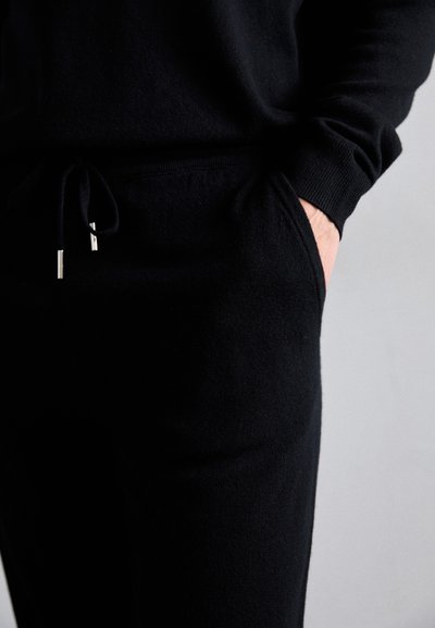 Black knit loungewear set featuring a drawstring waist, side pockets, and ribbed cuffs. Soft texture with a smooth finish.