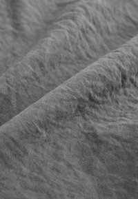 Grauer Stoff mit einer weichen, strukturierten Oberfläche, der dezente Falten und eine matte Oberfläche aufweist und Tonvariationen zeigt.