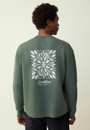 Grüner Strickpullover mit einem großen weißen Blumenmuster auf dem Rücken und Details mit der Aufschrift "République" und "Paris - Bloc 11."
