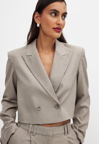 Cropped light gray blazer in textured fabric, featuring a double-breasted design with two buttons and sharp lapels. Tailored fit with pockets.