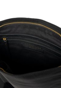 Interior de un bolso de cuero negro con un zipper dorado, que cuenta con múltiples compartimentos, incluyendo un bolsillo con zipper y una etiqueta de marca.
